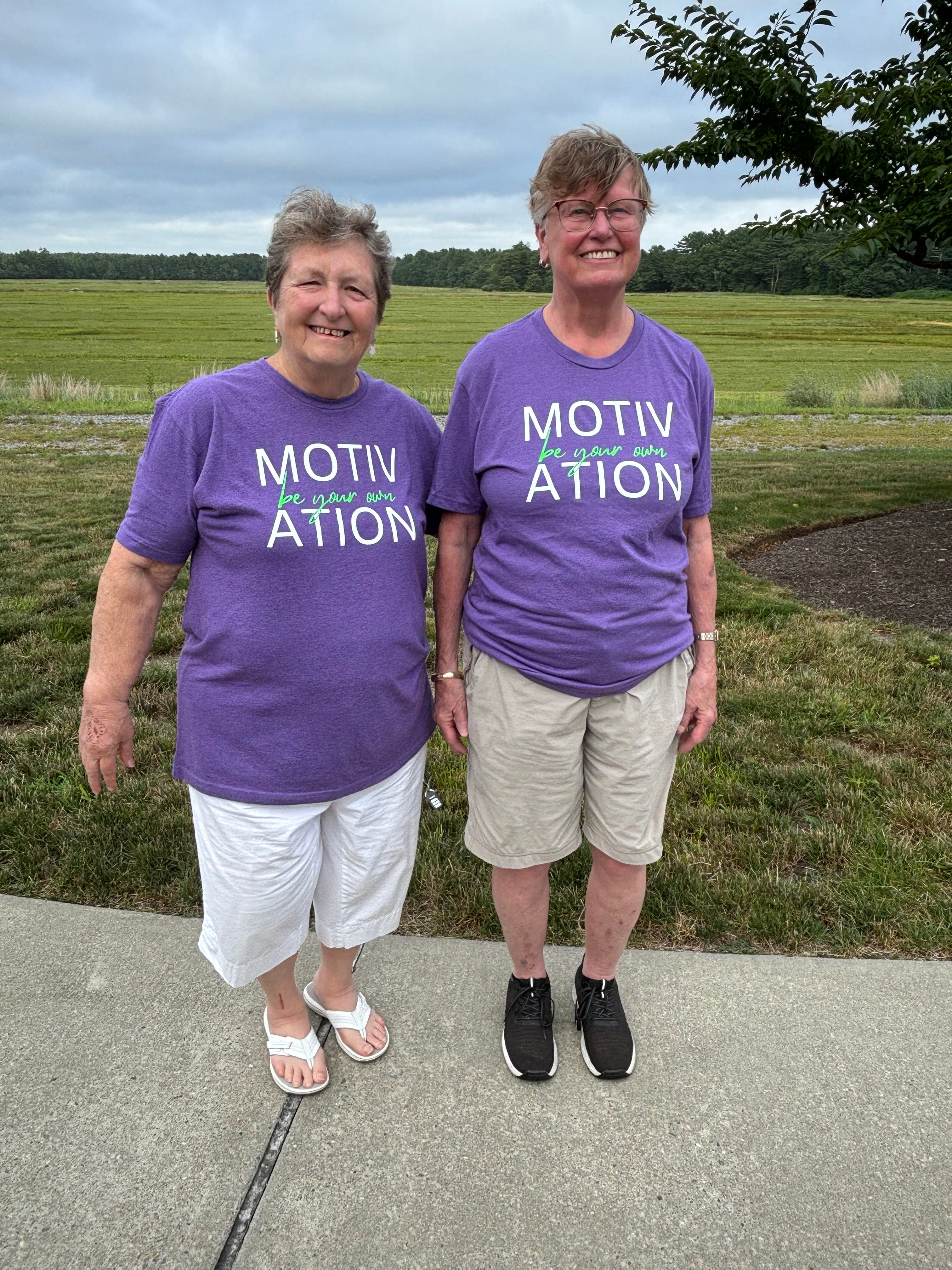 Judy Rego and Gayle Whittle, Moxie Mobility Training volunteers, wearing purple Motivation shirts outdoors