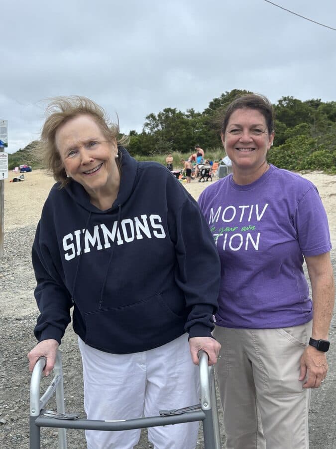 Kathy Clark with a senior client using a walker smiling together at a Southcoast Massachusetts beach during an accessible outing