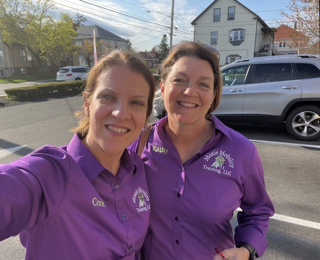 Kathy Clark and Corie Trezon of Moxie Mobility Training smiling in matching purple branded shirts