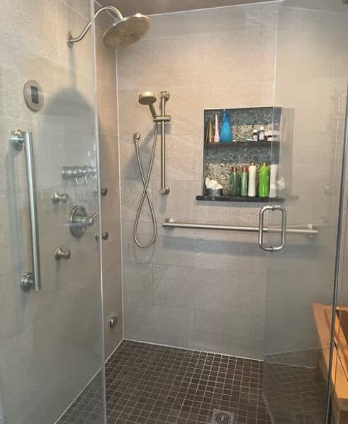 Modern walk-in shower with grab bars, handheld sprayer, and teak bench — home safety modifications for aging in place