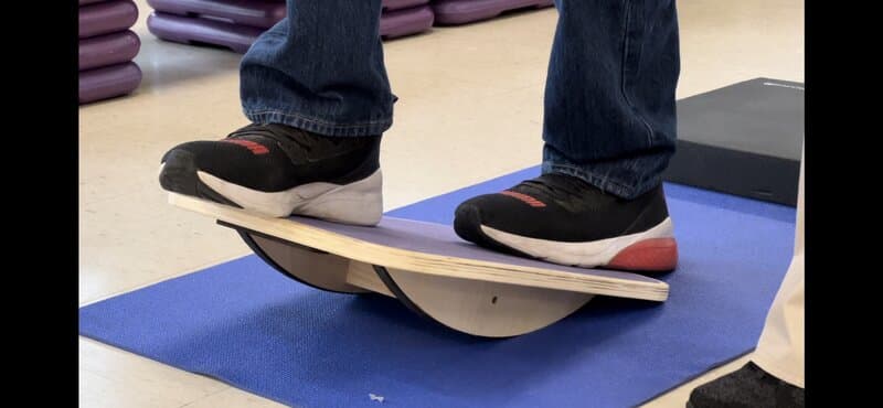 Senior woman performing a sit-to-stand chair exercise on a balance pad during a Moxie Mobility Training balance and circuit class